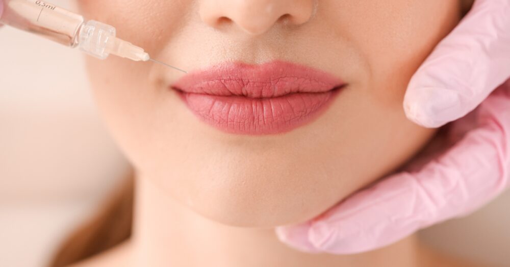 Woman receiving a lip filler treatment with a provider's gloved hands gently holding the chin area