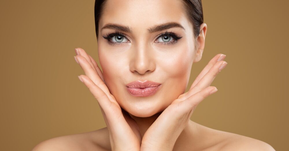 Woman with smooth, naturally full lips posing with her hands framing her face against a neutral background