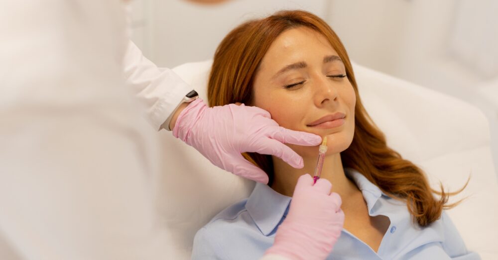 Woman receiving a cosmetic lip injection from a provider wearing pink medical gloves