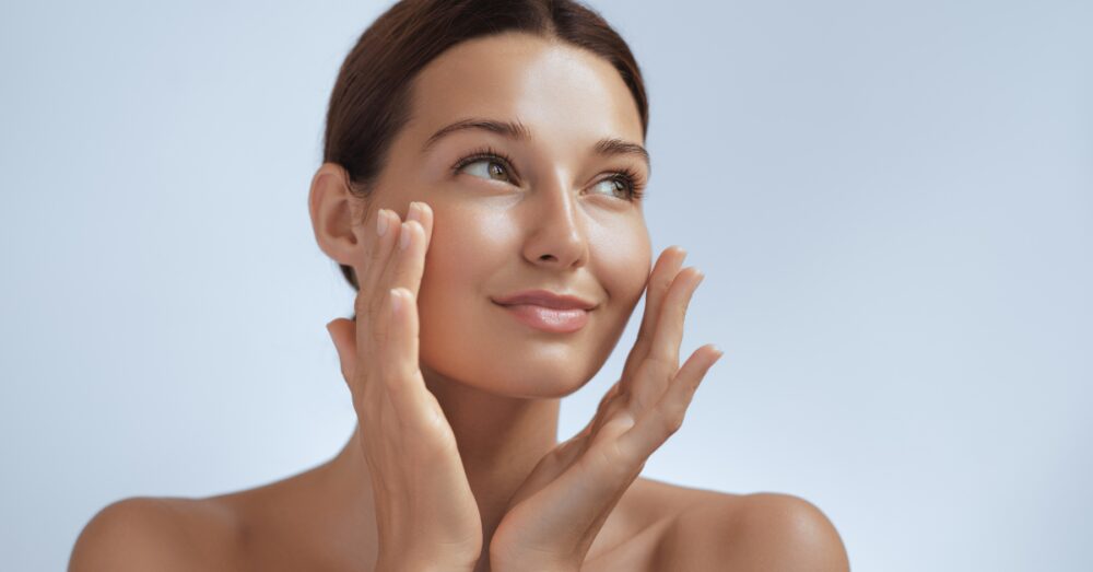 A woman with radiant, glowing skin touching the sides of her face